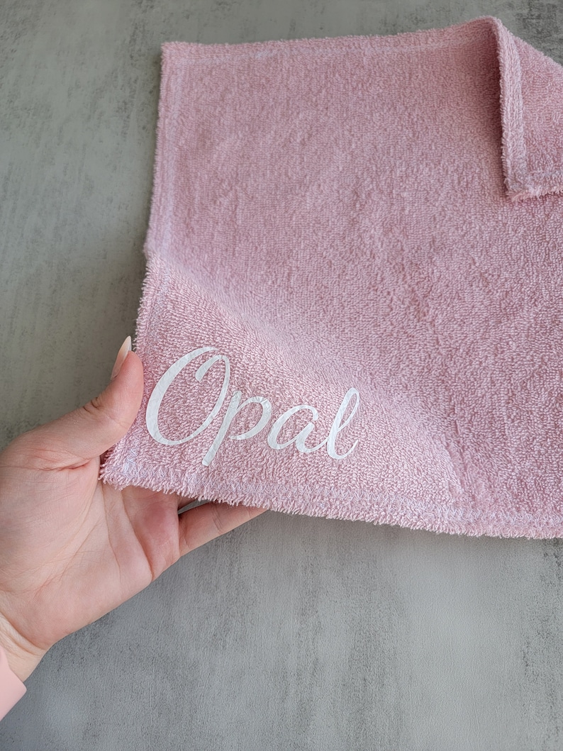 Op de afbeelding: Een roze handdoek met de naam "Opal" geborduurd in wit.