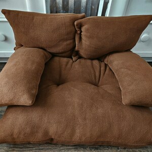 May include: A brown, plush floor cushion with two large pillows and two smaller pillows. The cushion is made of a soft, comfortable material and is perfect for lounging.