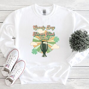 May include: White sweatshirt with a retro-style graphic design featuring a glass of dark beer and the text "Lovely Day for an Irish Stout".