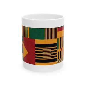 May include: A white ceramic mug with a colorful Kente cloth design. The design features a patchwork of geometric patterns in red, yellow, green, and black. The mug is cylindrical and has a standard handle.