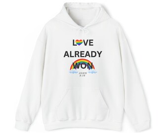 Puede incluir: Sudadera con capucha blanca con un corazón arcoíris y el texto "LOVE ALREADY WON" con un arcoíris y nubes debajo. El texto "JOHN 3:16" está debajo del arcoíris.