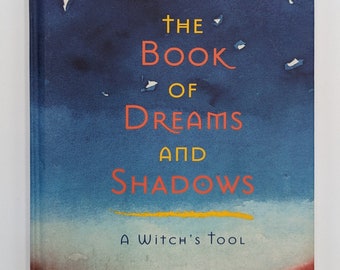 Op de afbeelding: Boekomslag met een aquarel-illustratie van een halve maan en sterren tegen een blauwe lucht. De titel is "The Book of Dreams and Shadows: A Witch's Tool" door Lady Raya.