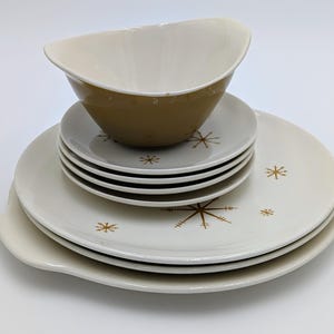 Peut inclure: Service de table vintage avec un grand saladier et plusieurs assiettes. Les assiettes sont blanches avec des motifs dorés en forme d'étoiles. Le saladier est vert olive à l'extérieur et crème à l'intérieur.