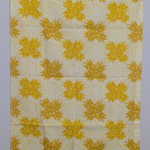 K&ouml;nnte beinhalten: Ein rechteckiger, cremefarbener Stoff mit einem sich wiederholenden Muster aus gelben Sternen. Jeder Stern ist mit kleinen wei&szlig;en floralen Details gef&uuml;llt. Der Stoff h&auml;ngt an einem transparenten Kunststoffclip.