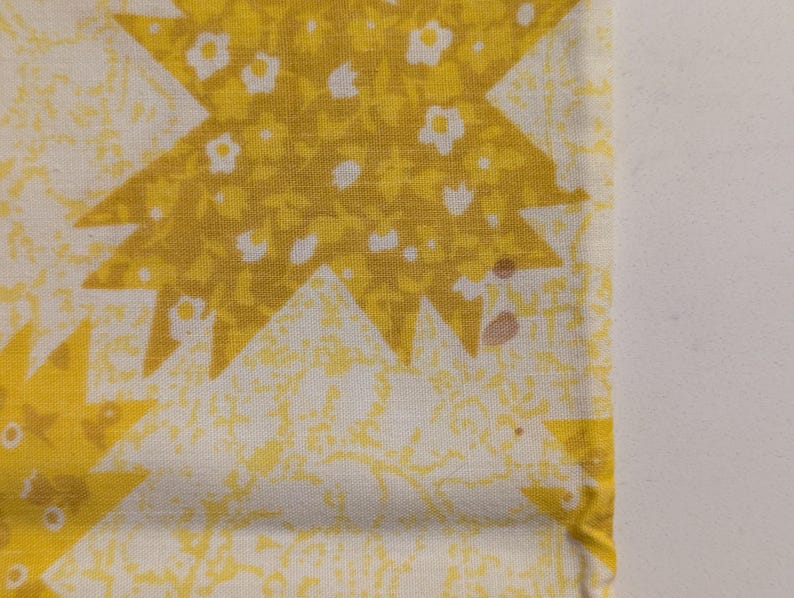 K&ouml;nnte beinhalten: Nahaufnahme eines Stoffabschnitts mit einem sich wiederholenden Sternmuster. Die Sternmuster sind gelb und mit winzigen wei&szlig;en Blumen gef&uuml;llt. Der Hintergrund ist hellgelb mit einem dezenten Blumendesign. Es gibt ein paar kleine braune Flecken auf dem Stoff.