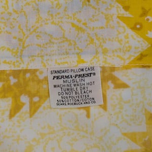 K&ouml;nnte beinhalten: Nahaufnahme eines gelb-wei&szlig; gemusterten Kissenbezugs. Der Kissenbezug hat ein Etikett mit der Aufschrift "STANDARD PILLOW CASE PERMA-PRESTO MUSLIN MACHINE WASH HOT TUMBLE DRY DO NOT BLEACH 50% POLYESTER 50% COTTON/COTON SEARS, ROEBUCK AND CO."
