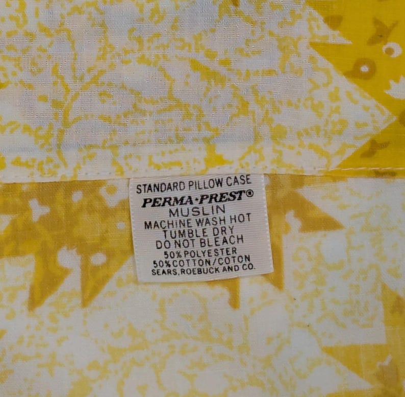K&ouml;nnte beinhalten: Nahaufnahme eines gelb-wei&szlig; gemusterten Kissenbezugs. Der Kissenbezug hat ein Etikett mit der Aufschrift "STANDARD PILLOW CASE PERMA-PRESTO MUSLIN MACHINE WASH HOT TUMBLE DRY DO NOT BLEACH 50% POLYESTER 50% COTTON/COTON SEARS, ROEBUCK AND CO."