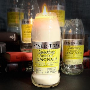 May include: A glass bottle candle shaped like a Fever-Tree Sparkling Sicilian Lemonade bottle. The candle is lit and the wax is melted. The label reads "Fever-Tree Sparkling Sicilian Lemonade with natural flavours including Sicilian lemons. Taste: Bright & Zesty. No artificial sweeteners. 6.8 fl oz (200 ml)"