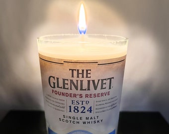 May include: A clear glass candle with a brown label that reads "The Glenlivet Founder's Reserve Est. 1824 Single Malt Scotch Whisky". The candle is lit and the flame is visible.