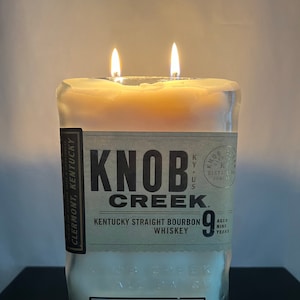 Peut inclure: Un bocal à bougie en verre transparent avec une étiquette qui indique "Knob Creek Kentucky Straight Bourbon Whiskey 9 Years Aged". La bougie est allumée avec deux flammes.