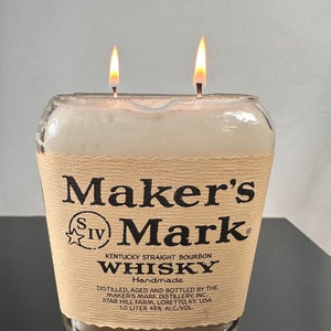 May include: A brown glass candle shaped like a Maker's Mark whiskey bottle with two wicks burning. The label reads "Maker's Mark Kentucky Straight Bourbon Whiskey Handmade Distilled, Aged and Bottled by the Maker's Mark Distillery, Inc. Star Hill Farm, Loretto, KY. USA 1.0 Liter 45% Alc./Vol."