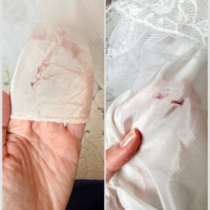 May include: A white garment featuring layers of sheer tulle fabric and a smooth, opaque lining. The fabric displays visible signs of wear, including small tears and frayed areas in the delicate netting and the underlying satin-like material.
