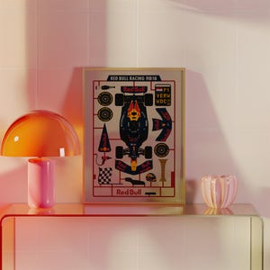 May include: A framed print featuring a Red Bull Racing RB18 Formula 1 car schematic. The print includes the Red Bull logo and text, with a detailed breakdown of car components. The color scheme is primarily navy blue, red, and yellow.