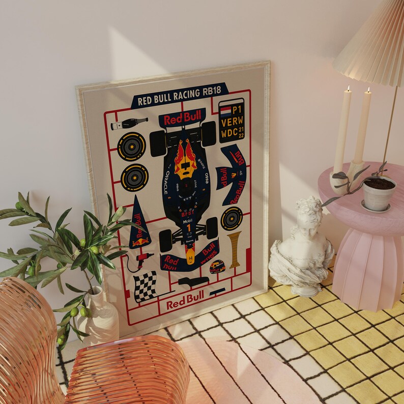 May include: A framed print featuring a schematic of a Red Bull Racing RB18 Formula 1 car. The design includes the Red Bull logo, car components, and text. The print is displayed on a wall, with a lamp and small table nearby.
