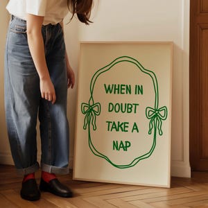 Op de afbeelding: Een ingelijst print met een groene omtrek van een strik en de tekst "When in doubt take a nap".