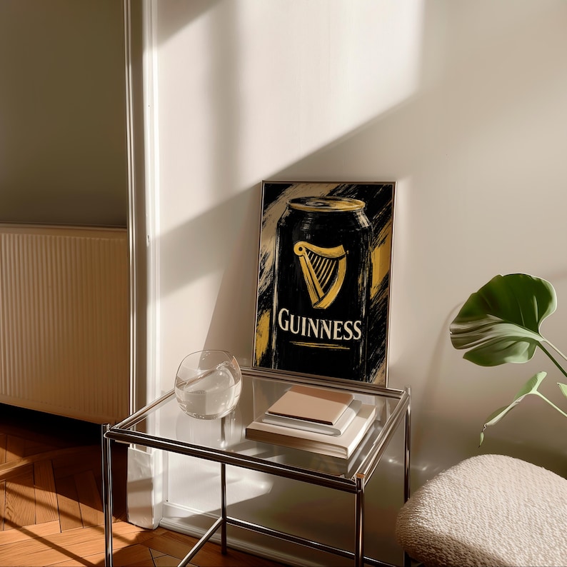May include: A framed art print featuring a black Guinness can design with gold accents. The Guinness logo, a golden harp, is prominently displayed. The artwork is set against a textured, abstract background. The print is displayed on a glass-topped table.