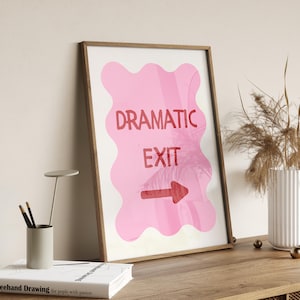 Puede incluir: Un cuadro enmarcado con las palabras "DRAMATIC EXIT" en rojo sobre un fondo rosa ondulado. Una flecha roja indica la dirección de salida. El cuadro está en un marco de madera.