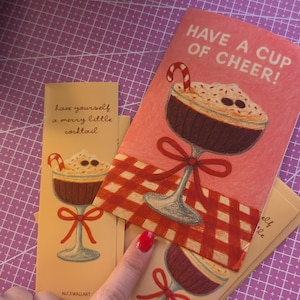 May include: Cards with illustrations of a cocktail in a stemmed glass, with a candy cane and whipped cream. The cards have the phrases "Have a cup of cheer!" and "Have yourself a merry little cocktail."