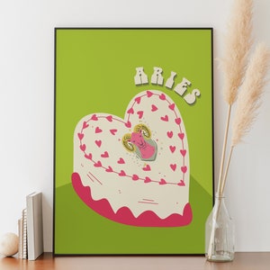 May include: A green background with the word "Aries" in pink and white letters. A heart-shaped cake with pink frosting and a pink ram in the center. The cake is decorated with pink hearts.