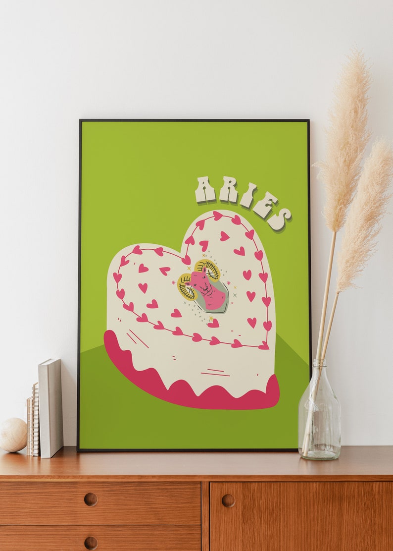 May include: A green background with the word "Aries" in pink and white letters. A heart-shaped cake with pink frosting and a pink ram in the center. The cake is decorated with pink hearts.