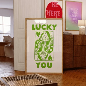 May include: A white poster with green text that reads "LUCKY YOU" and a green illustration of the Queen of Hearts playing card.