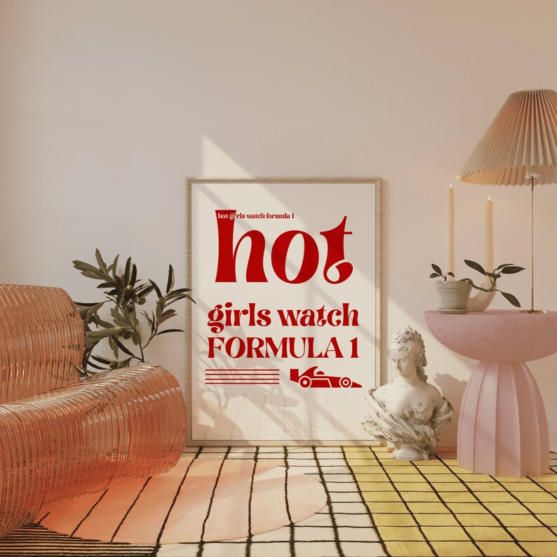 May include: A white framed poster with red text that reads "hot girls watch formula 1". The poster is hanging on a wall in a room with a pink and yellow checkered floor. There is a pink side table with a potted plant and a white bust sculpture on the table.