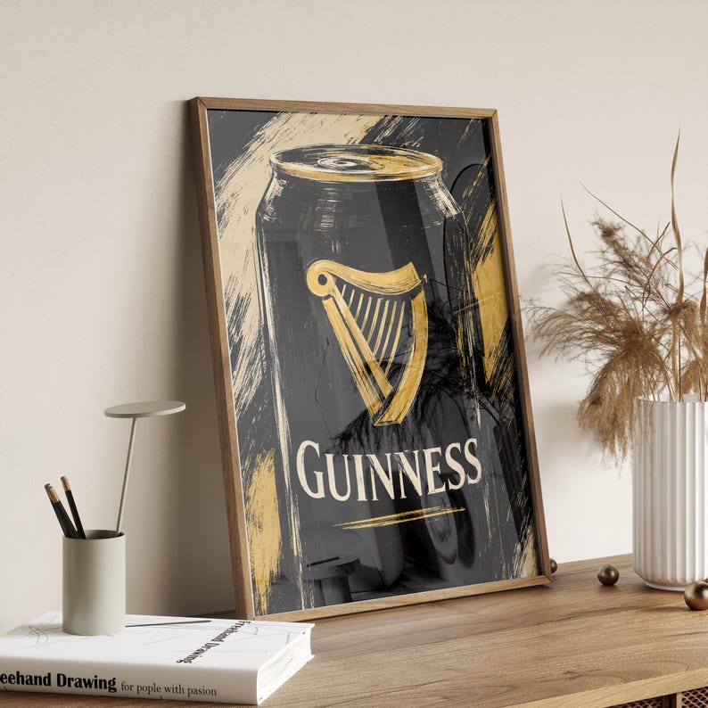 May include: A framed print featuring a stylized Guinness can. The artwork showcases a black can with a gold harp logo and the Guinness name in white. Gold brushstrokes add texture to the background.