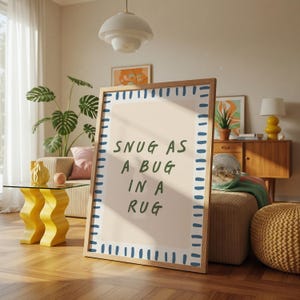 Peut inclure: Une affiche encadrée en bois avec le texte "SNUG AS A BUG IN A RUG" en vert. L'affiche a un fond rose clair et une bordure bleue pointillée. L'affiche est présentée dans un salon avec une table jaune et une plante.