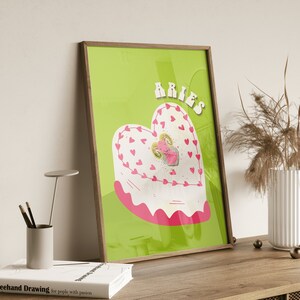 May include: A green background with the word "Aries" in pink letters. A pink heart-shaped cake with a pink ram inside. The cake is decorated with white frosting and pink hearts.