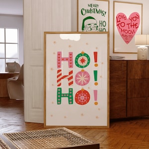 Peut inclure: Une impression encadrée avec un fond blanc et le mot "HO!" en grandes lettres colorées. Les lettres sont décorées de cannes en sucre, de flocons de neige et de boules. L'impression est entourée d'un cadre en bois.