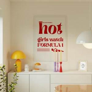 May include: A white framed poster with red text that reads "hot girls watch formula 1" with a red illustration of a race car. The poster is hanging on a white wall above a white dresser with a yellow lamp, a white decorative object, and a small book.