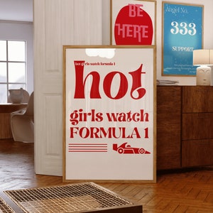 May include: A white poster with red text that reads "hot girls watch formula 1" and a red illustration of a racing car. The poster is framed in wood.