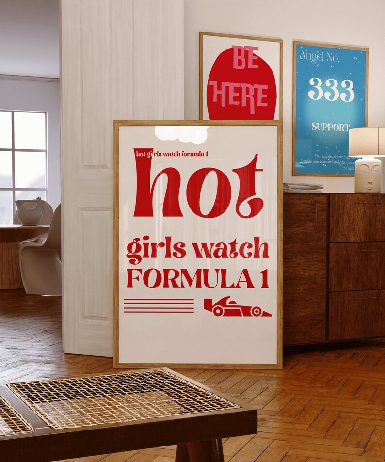 May include: A white poster with red text that reads "hot girls watch formula 1" and a red illustration of a racing car. The poster is framed in wood.