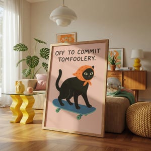 May include: A framed print shows a black cat wearing an orange headscarf, skateboarding on a blue board. The text "OFF TO COMMIT TOMFOOLERY" is above the cat on a pink background. The print is in a wooden frame.