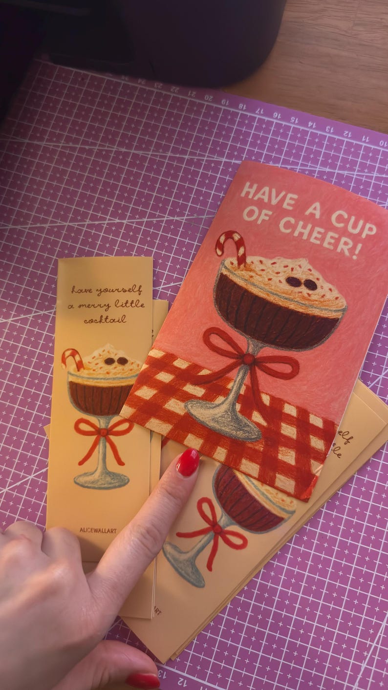 May include: Cards with illustrations of a cocktail with a candy cane, whipped cream, and chocolate sprinkles. The cards have the phrases "Have a cup of cheer!" and "Have yourself a merry little cocktail."
