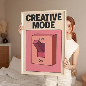 Może przedstawiać: Oprawiony plakat z napisem "CREATIVE MODE" pogrubionymi czarnymi literami. Plakat przedstawia różowo-pomarańczową grafikę przełącznika z etykietami "ON" i "OFF". Rama jest w kolorze jasnobeżowym.