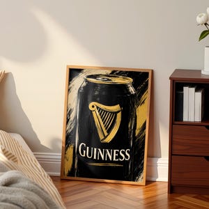 May include: A framed art print featuring a stylized depiction of a Guinness can. The artwork showcases a black can with a gold harp logo and the word "Guinness" in white. The background has gold and black brushstrokes.