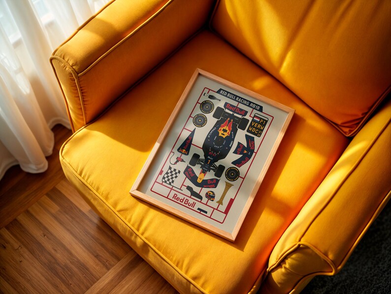 May include: A framed print featuring a Red Bull Racing 2018 Formula 1 car design. The artwork, with a light wood frame, is displayed on a yellow upholstered armchair. The print includes the Red Bull logo and car components.