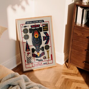 May include: A framed print featuring a schematic of a Red Bull Racing RB18 Formula 1 car. The print includes the Red Bull logo and various car components in a grid-like layout. The color scheme is primarily navy, red, and yellow.