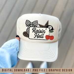 May include: A cream-coloured trucker hat with a graphic design. The design includes a black and white chequered bow, a leopard print heart, a star, a pool ball, and two red cherries. The text "Raisin' Hell" is also featured.