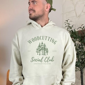 May include: A light beige hoodie with a green graphic of trees and the text "Woodcutting Social Club Est. 2001 Draynor Village" printed on the front.