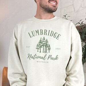 May include: A light beige sweatshirt with a green graphic design that says "Lumbridge National Park Est. 2001 Mistralin".