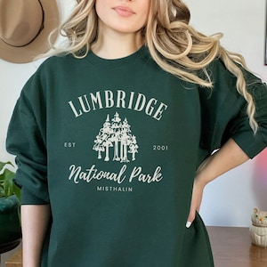 May include: A dark green sweatshirt with a white graphic design that says "Lumbridge National Park Est. 2001 Misthalin". The graphic features a stylized image of a group of trees.