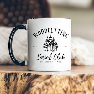 May include: White ceramic mug with a black rim and handle. The mug has a black and white logo that says "Woodcutting Social Club Est. 2001 Draynor Village".