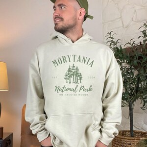 May include: A light beige hoodie with a green graphic print that says "Morytania National Park, Est. 2004, The Haunted Woods".