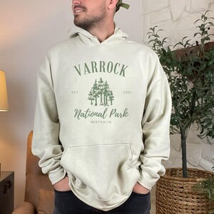 May include: A light beige hoodie with a green graphic print that says "Varrock National Park Est. 2001 Misthallin".