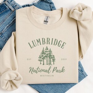 May include: A beige sweatshirt with a green graphic design that says "Lumbridge National Park Est. 2001 Misthalin".