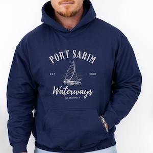 May include: Navy blue hooded sweatshirt with a white sailboat graphic and the text "PORT SARIM WATERWAYS ASGARNIA". The sweatshirt has a front pocket and a drawstring hood.