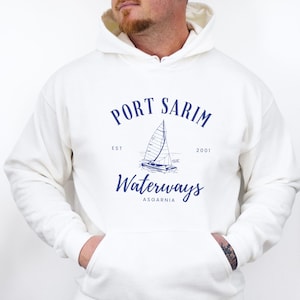 May include: White hooded sweatshirt with a navy blue graphic that reads "Port Sarim Waterways Asgarnia" with a sailboat illustration. The sweatshirt has a front pocket and a drawstring hood.