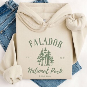 May include: A beige hoodie with a green graphic design that says "Falador National Park Est. 2001 Asgardia".